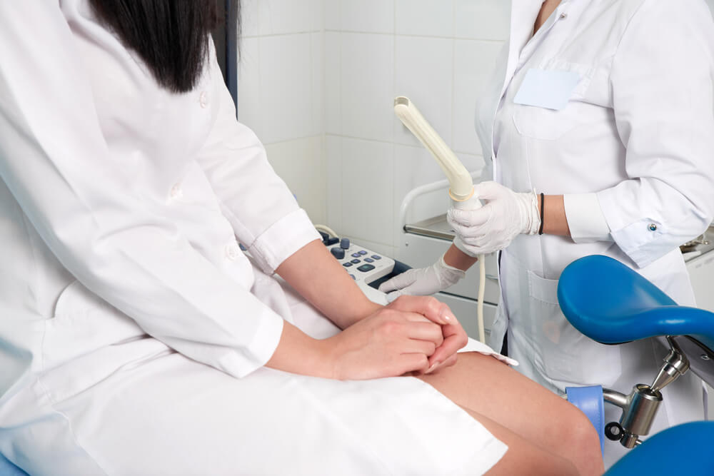 Gynecologist ready to do transvaginal ultrasound with wand and exam a woman

