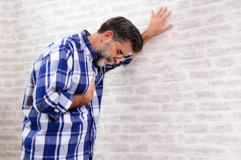 Ill senior man touching chest and stick to the wall. Matur Man having a heart attack