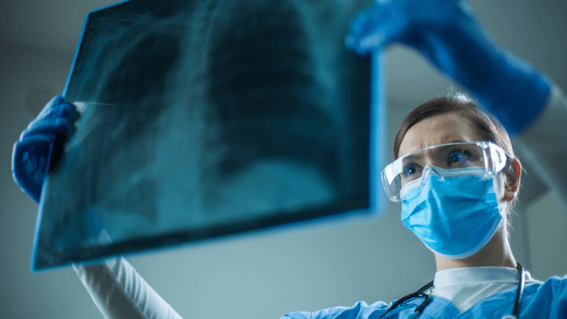 Female pulmonologist or oncologist holding chest X-ray scan,inspecting COVID-19 patient lungs,wearing PPE uniform,Coronavirus acute respiratory new virus disease infection causing breathing problems