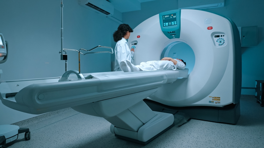 Patient in white clothes undergoes magnetic resonance imaging scan, laying down on bed for CT or PET scan