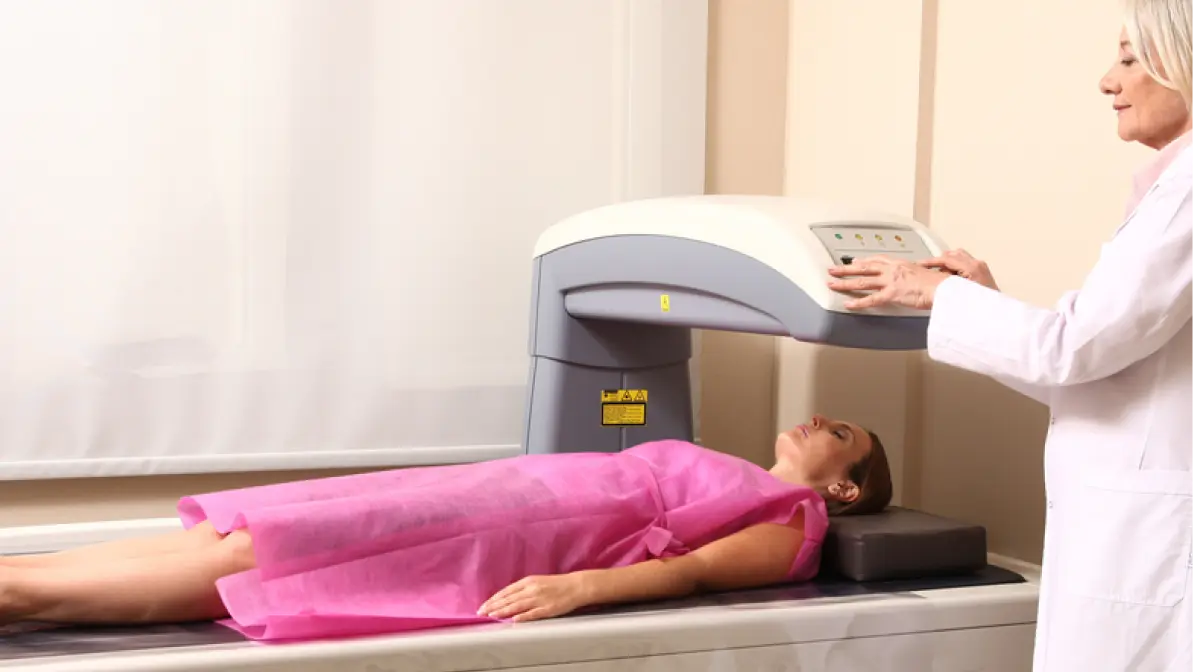 Female doctor examining woman in 40s at Bone Densitometer Machine.